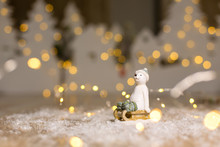Decorative Christmas-themed Figurines. The Statuette Of A Polar Bear Sits On A Wooden Sled, In A Knitted Hat And Socks. Christmas Tree Decoration. Festive Decor, Warm Bokeh Lights.