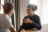 Fototapeta  - Serious indian mentor worker talk to female colleague teach intern
