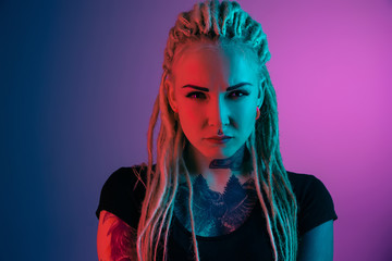 Caucasian young woman's portrait on gradient background in neon light. Beautiful female model with unusual look. Concept of human emotions, facial expression, sales, ad. Looking at camera serious.