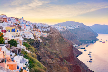 Wall Mural - Picturesque cityscape of Oia village on Santorini Island with traditional white architecture over the Caldera mountains in Aegean sea at sunset,  Greece. Scenic travel background.