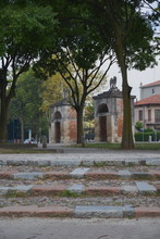 View From The Inside Of The Park To The Gate: Stone Guards, Each With A Stone Eagle. Trees In The Park, Climbing Steps. Gate And Entrance To The Park Of The City Of Mantova, Italy.