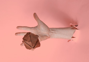 Wall Mural - Female hand throws crumpled ball of paper through the torn pink paper background. Minimalistic idea concept