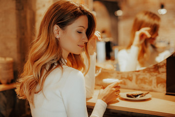 attractive girl drinks her delicious aromatic coffee with milk.cozy coffee shop, people drink morning coffee on a warm autumn day. girl sitting by the mirror on the bar counter with latte. vintage ins