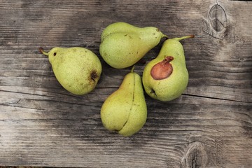 four green pears lie on a wooden surface, on one of the pears a brown speck looks like a duck