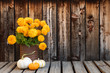 Rusty can filled with a bunch of bright orange marigold flowers next to three small fall gourds on a rustic plank table with room for copy