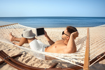 Wall Mural - Young man with tablet in hammock on beach