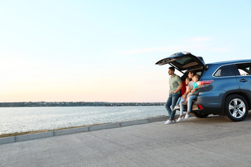 Poster - Happy young family sitting in car trunk on riverside