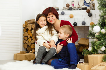 Wall Mural - Family on Christmas eve at fireplace. Mother and little kids opening Xmas presents. Children with gift boxes. Living room with traditional fire place and decorated tree. Cozy winter evening at home.