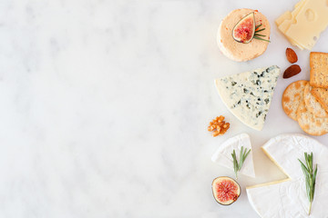 Aufkleber - Border of a selection of cheeses, figs, nuts and crackers. Top view on a white marble background with copy space.