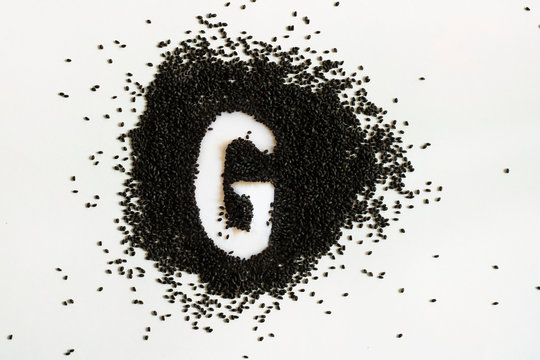 Handful of sweet basil black seeds, letter G uppercase of English alphabet on white background. Black and white. Lettering. Typography. Healthy and super food. Horizontal