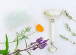 Gua sha stone and jade roller arranged with California poppy and colorful wildflowers / still life on white marble background / green natural holistic beauty concept