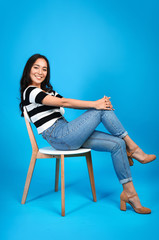 Wall Mural - Beautiful Asian woman sitting on chair against color background