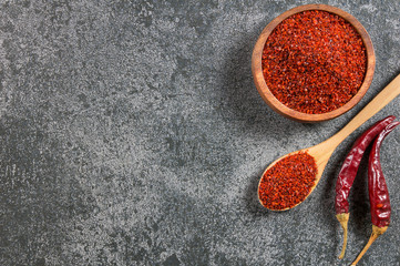 Top view red dried crushed hot chili peppers and chili flakes or powder in wooden spoon and bowl on grey rustic background, healthy turkish spice