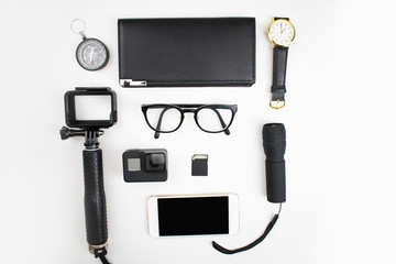 Top view of the black accessories for tourists with a camera, glasses, flashlight, compass, wallet and smartphone on a white background.