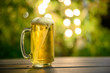 © Lowpower - A glass of cold beer with a foam on top Placed on a table in the garden, the background is a green tree and has beautiful bokeh at dusk.