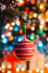 Christmas ball hangs on a decorated fir tree against the background of burning bokeh lights at night.