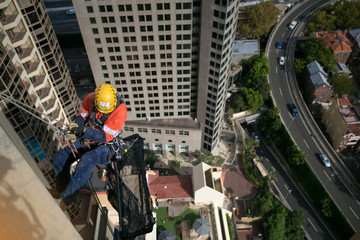 Wall Mural - Abseiler wearing full body safety harness helmet fall head protection equipment working at height abseiling after completed a task high rise building Sydney CBD cityscape, Australia  