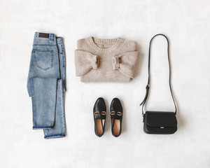 Wall Mural - Blue jeans, beige knitted oversize sweater, small cross body bag, black loafers or flat shoes on grey background. Overhead view of women's casual day outfit. Flat lay, top view. Women clothes.