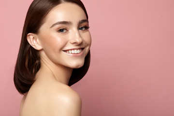beautiful smiling woman with clean skin, natural makeup and white teeth on a pink background
