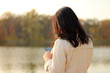 © PeterPike - White dark haired girl looks at the cellphone and swipes a finger on the phone screen on a background of an autumn lake