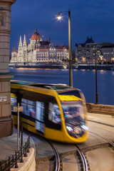 Wall Mural - Budapest, Hungary - Yellow tram on the move at Clark Adam Square with illuminated Parliament building at background at blue hour