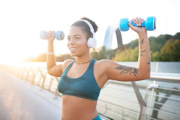 Wall Mural - Dark-skinned woman wearing earphones working out her muscles