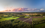 Fototapeta Do pokoju - Aerial view on impressive storm clouds over forest in colorful sunset colors. Dark storm clouds covering the rural landscape. Intense rain shower in distance. 