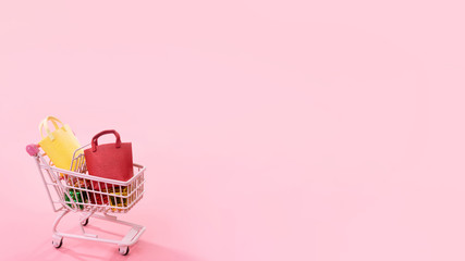 Annual sale shopping season concept - mini pink shop cart trolley full of paper bag gift isolated on pale pink background, blank copy space, close up