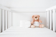 Brown Teddy Bear With White Diaper Sitting In Baby Bed.