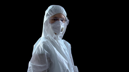 Wall Mural - Lab worker in protective suit and mask looking at camera against dark background
