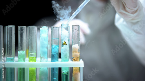 Fotografía Lab worker pouring liquid in test tube with biohazard symbol, modern weapon