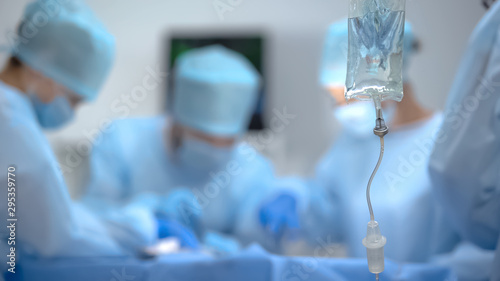 Cuadros en Lienzo Medical drip bag on background of surgeon team working in operation room