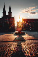 Wall Mural - Old historic town with a cathedral and fountain with a long shadow on the cobble stone with moody and colorful sunset light. Empty urban. Historic City center, Altstadmarkt in Braunschweig, Germany