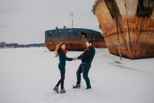 Loving Young Couple Man And Woman Walk In The Winter On A Frozen River Near The Ships In Winter.