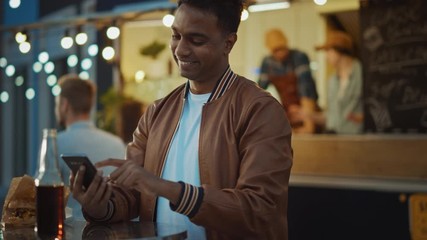 handsome young indian man is using a smartphone while sitting at a table in a outdoors street food c