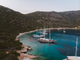Wall Mural - Aerial drone perspective of luxury Turkish gulets and yachts in the deep blue and turquoise waters of the mediterranean sea. The bay and cliffs protect the boats from the strong winds.