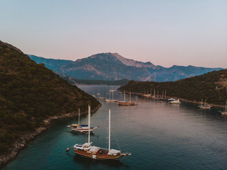 Wall Mural - The sun setting over a quiet bay near Fethiye, Turkey. The traditional Turkish gulets line the shore with the mountainous coastal landscape in the background. 