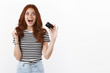 Cheerful thrilled cute ginger girl triumphing, pump her fist joyfully, scream from excitement and joy, showing credit card, react on cool new online banking feature, standing white background
