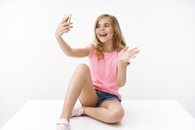 Cheerful Enthusiastic Happy Blond Teenage Girl Sitting Crossed Legs On Floor, Hold Smartphone, Record Blog, Communicate Father Abroad, Taking Selfie, Waving Hand Greeting Say Hi Mobile Phone
