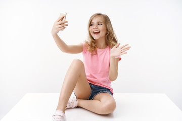 cheerful enthusiastic happy blond teenage girl sitting crossed legs on floor, hold smartphone, recor
