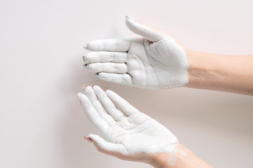 Portrait of a cute girl posing in a clay mask with clay hands in a white coat and a towel on her head posing with outstretched arms. The concept of cosmetics and beauty.