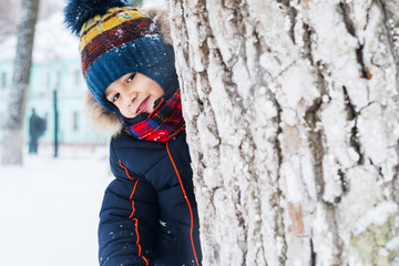 Wall Mural - cheerful boy looks out from behind a tree. winter walk