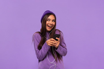 pretty african-american girl in a hat and sweater listening to music on a mobile phone with wired he