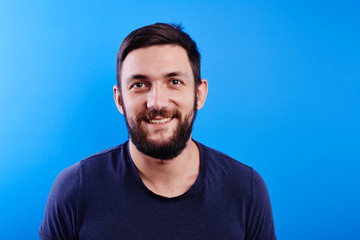 Wall Mural - Portrait of toothy smiling and joyfully laughing handsome caucasian brutal bearded man dressed in casual isolated on blue background