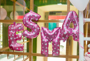 E, s, m, a, letters made with balloons. White hearts inside the balloon . Esma written in balloon in pink color .