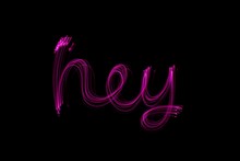 Long Exposure Photograph Of The Word 'hey' In Pink Neon Colour In An Abstract Swirl Pattern Against A Black Background. Light Painting Photography.