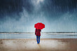 Lonely woman with red umbrella is standing in the rain watching the sea