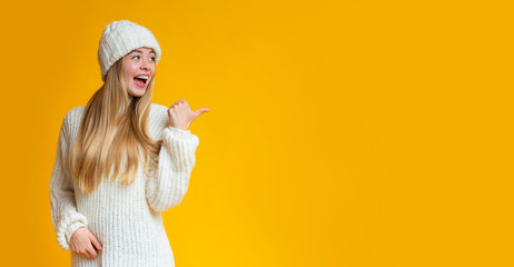 cheerful girl pointing with thumb at empty space
