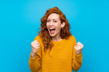 Wall Mural - Redhead woman with yellow sweater celebrating a victory in winner position