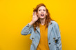 Redhead woman over isolated yellow background listening something